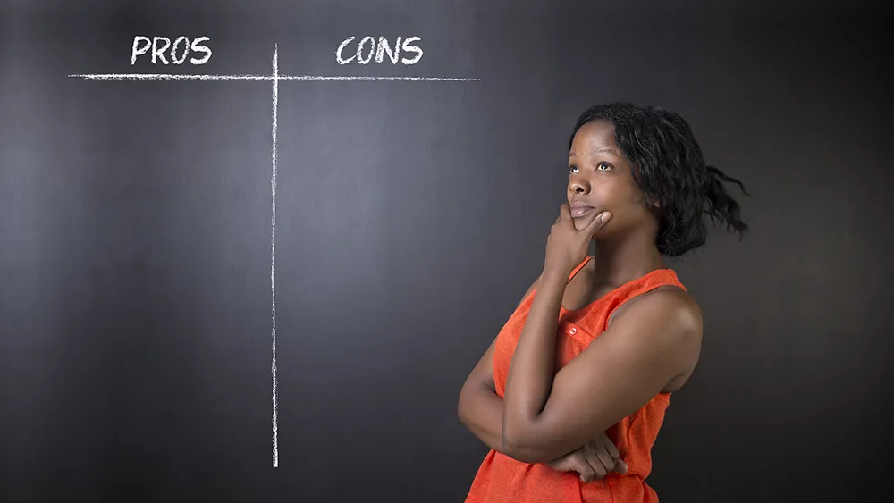 A solopreneur stands thinking in front of a blackboard with two columns labeled "Pros" and "Cons," both columns empty.