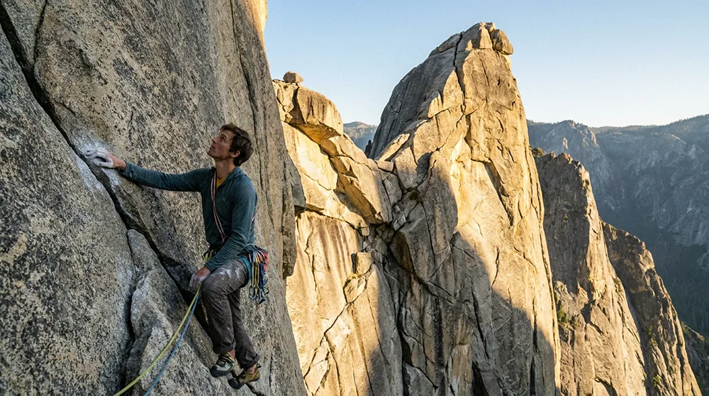 A solopreneur ascends a steep rock face using safety ropes and gear, with rugged mountain peaks and a clear sky in the background—symbolizing the challenges and triumphs of online business growth.